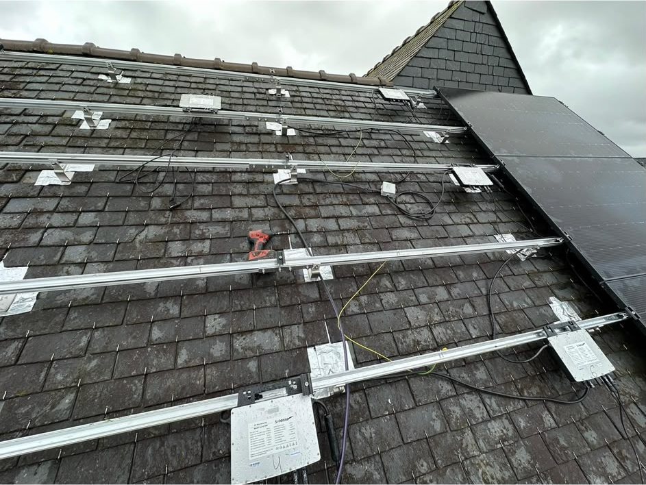 Pose des rails de fixation et des micro-onduleurs sur une toiture en ardoise avant installation des panneaux solaires